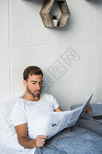 穿着白色T恤坐在床上阅读商业报纸背景图片