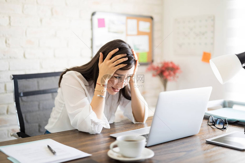 精神紧张的年轻女商人用头抱看台桌上的笔记图片