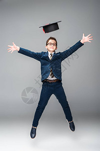 身着商人服装的中学生穿着毕业帽跳跃图片