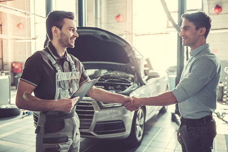 身穿制服的英俊年轻汽车机修工和一个客户握手笑着微笑图片