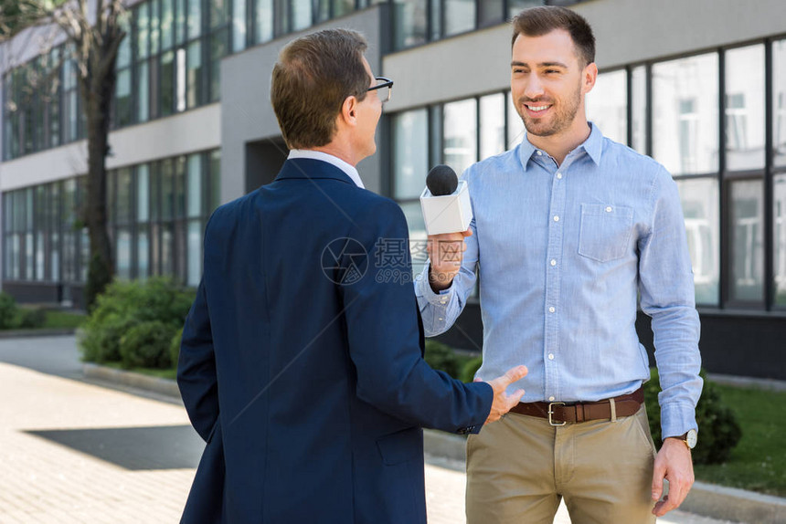 专业微笑记者用麦克风采访成功的成熟商人图片