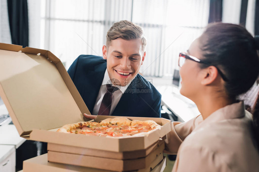 年轻女商人拿着披萨盒和笑的商人看着图片