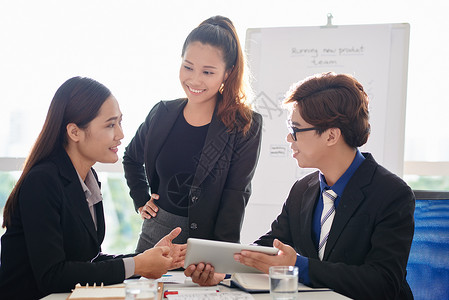 亚洲年轻商人在带全景窗户的现代会议室工作会议期间讨论数字平板电脑屏幕图片