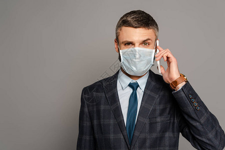 穿着医疗面具的英俊帅气商人在灰色背景上用图片