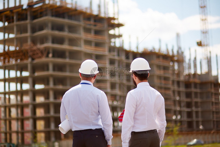 戴着头盔和正装的男建筑师看着未完工的建筑图片