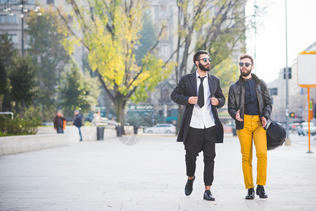两位年轻的留着胡子的金发黑现代商人走在城市背光中图片