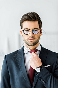 穿着正式穿戴和眼镜调整领带的英俊商人图片