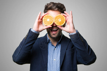 年轻人用灰色背景上的橘子遮住眼睛图片
