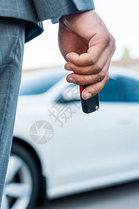 手持汽车钥匙和背景车辆的商人的部图片
