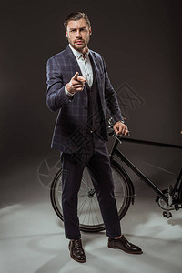 身穿西装身着重男装的青年男子在黑色自行车旁边站着时用照图片
