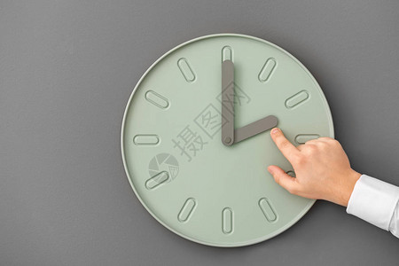 在灰色背景下指着时钟的人时间管理概念图片