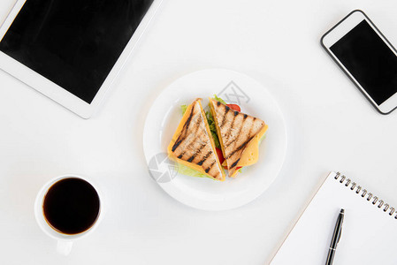 餐盘上美味三明治咖啡带笔的记本智能手机和工作场所图片