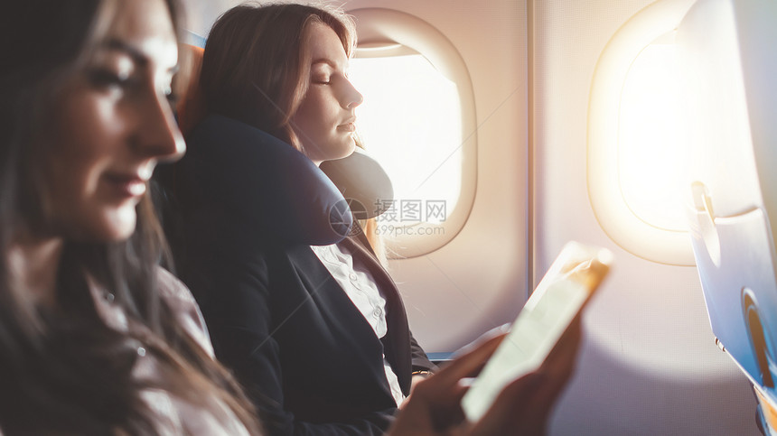 两个女乘飞机去出差一个女人在读智能手机电子书图片