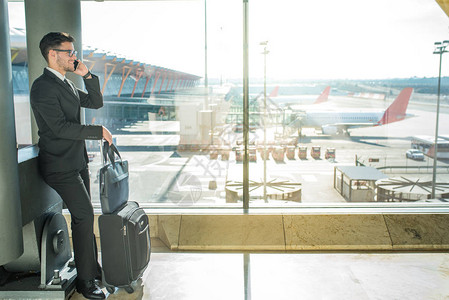 英俊的商人站在机场靠近终端窗口的机场等待他的飞行AC549图片