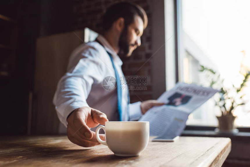 集中的商人早上在厨房看报纸喝咖啡时在图片