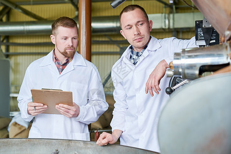 两名身穿实验室外套的男子在现代烘焙店工作时讨论咖啡加图片