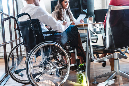 青年残疾商人坐在轮椅上与办公室同事一起工作的年轻残图片