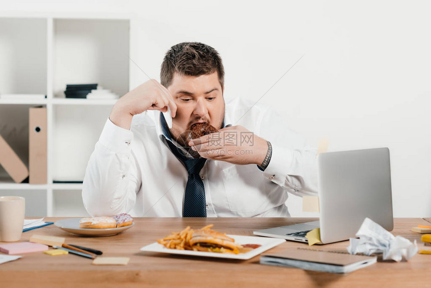 超重量体重商人在工作场所吃甜圈图片