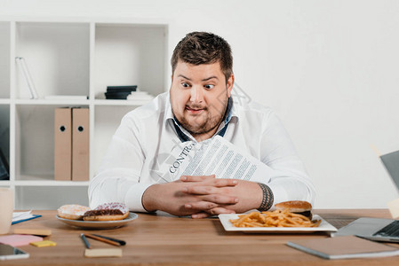 超重饥饿的商人选择甜圈或汉堡图片