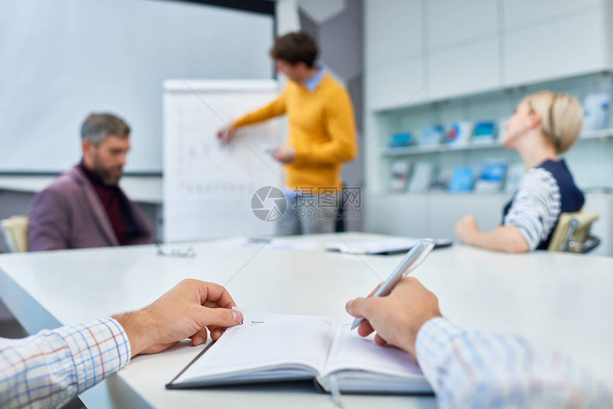 无法辨认的经理在工作会议期间坐在会议室桌子上时作必要笔记图片