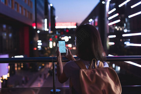 背着包和智能手机在屏幕上贴有天pe标志的双手站在夜市图片
