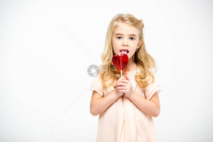 可爱的小女孩吃心形棒糖看着在白色上图片