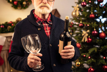 圣诞节持葡萄酒瓶和葡萄酒杯的年长男图片