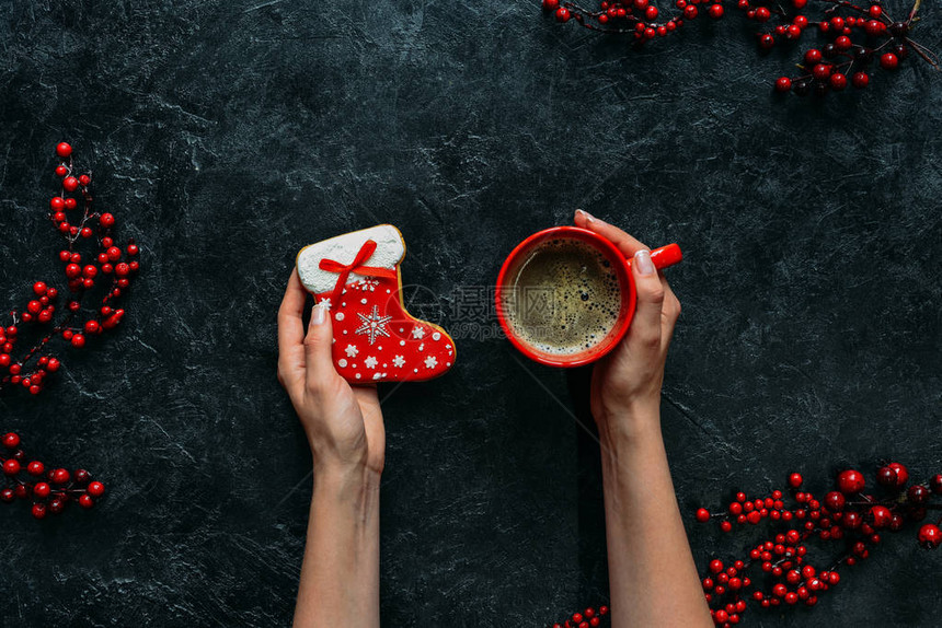 在黑桌顶上用装饰浆果握着姜饼和圣诞节丝袜和咖啡杯的女图片