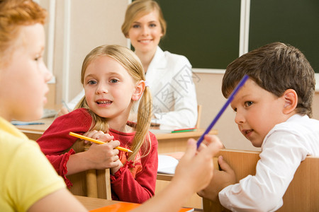 小学生坐在教室里和他们的老师在后面说话的肖像图片