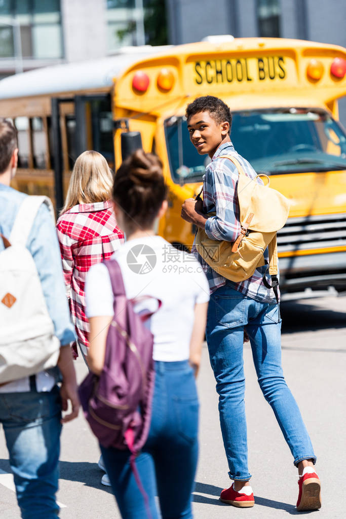 英俊的非洲少年男学生与同班学步行到校车图片