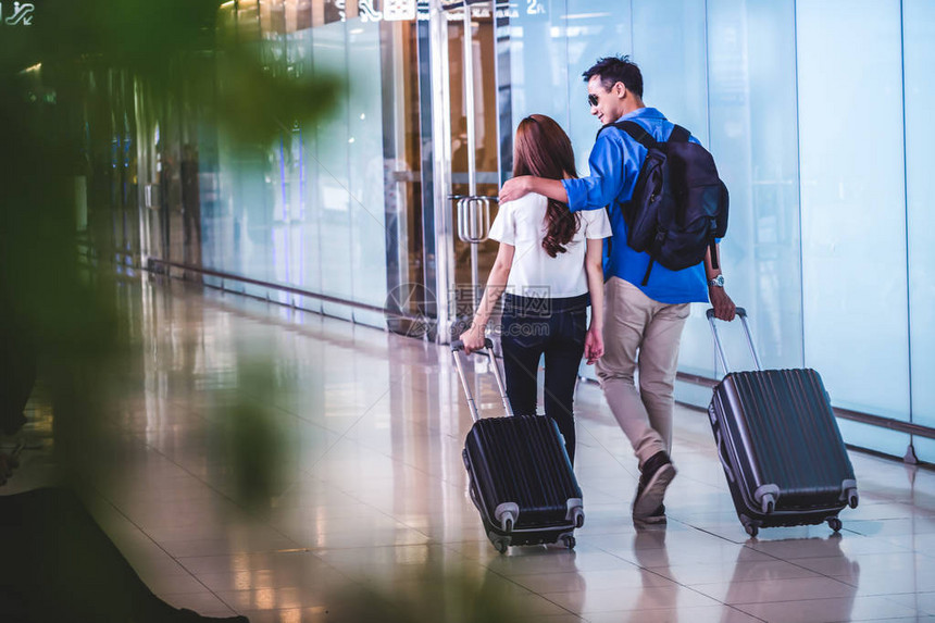 亚洲夫妇旅行者带着手提箱在现代机场行走旅行和交通概念图片