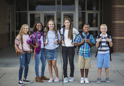 在校舍前微笑的青春期前学生的大群肖像一群背着包准备上学的不同孩图片