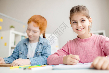 带着牙笑的可爱女孩看着镜头与同学一起上课图片