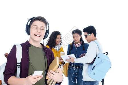 英俊的青少年学生耳机和智能手机在白人与朋友就背景聊天时被隔图片