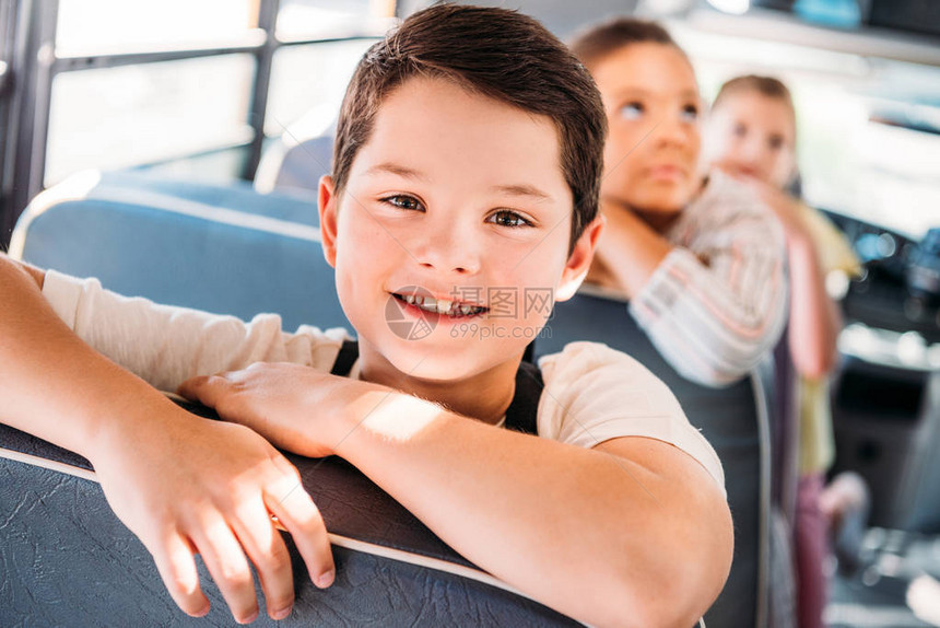 与背景模糊的同学一起坐在校车上的微笑着的小男图片