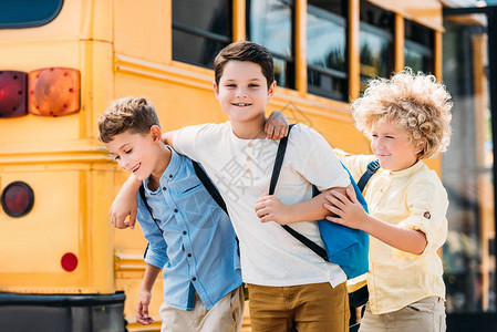 在校车前玩得开心的可爱小男孩们在图片