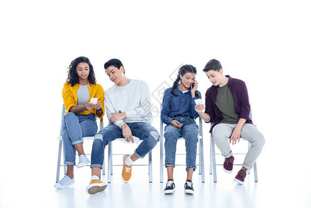 一群青少年学生使用智能手机在白色隔离椅上图片