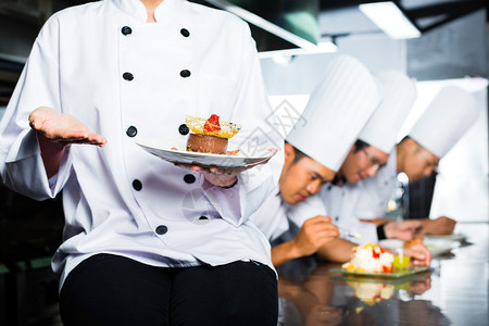 亚裔印度尼西亚厨师和其他厨师一起在餐馆或旅馆做饭烹饪最后菜图片