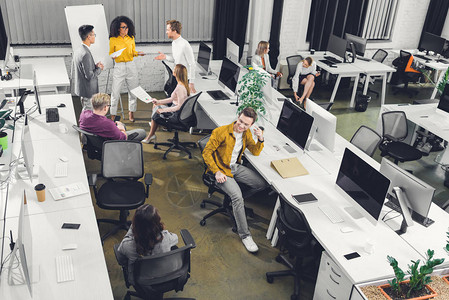 开放空间办公室与纸张和计算机一起工作的年轻商业同事的高角度视角图片