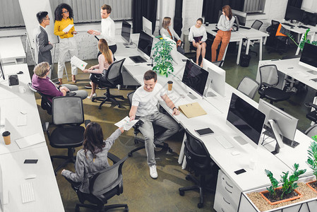开放空间办公室与纸张和计算机一起工作的专业年轻同事的高角度视角水图片