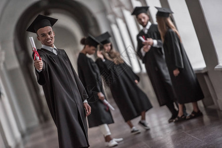 穿着学术着装的成功毕业生在大学厅里说话图片