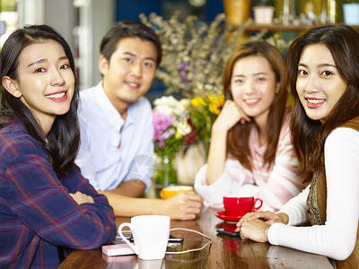 四组快乐的亚裔年轻成年男女在咖啡店聚会时微笑着看摄影机背景图片