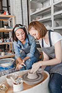 两个女朋友在陶工坊制作陶轮制作粘土手工艺品时微笑和交谈友图片