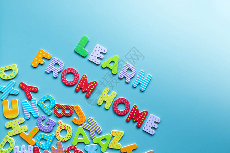 从家里学习的彩色木制字母和蓝色背景上散落的字母的单词图片