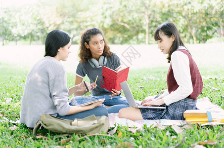 一群坐在户外草地上的年轻人正在公园里看书和一起使用笔记本多民族和多样图片
