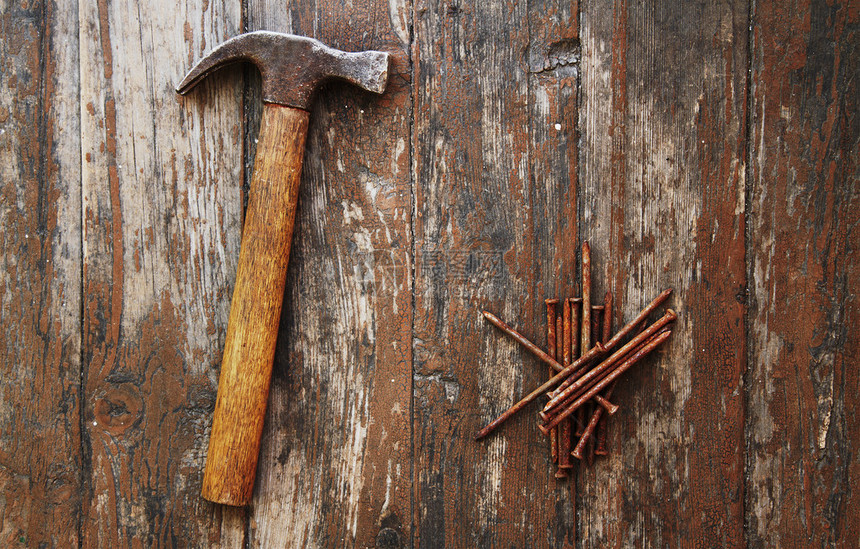 木制背景上的旧生锈钉子和锤子图片