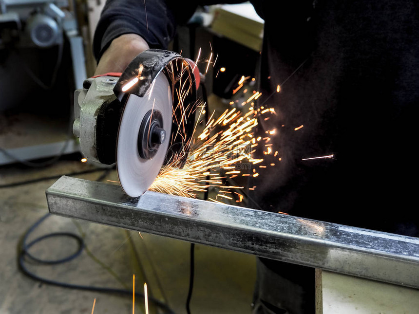 一个在工厂钢铁结构上使用电磨机工具的男人图片