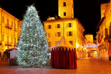城市广场上的圣诞大树照亮在意大利北部阿尔巴历史中心古塔前图片