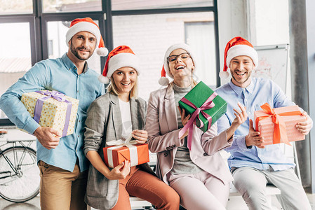 戴着圣诞帽的快乐同事拿着礼物在办公室图片