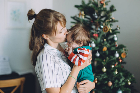 母亲在圣诞树和家里的家庭节日上抱着可背景图片